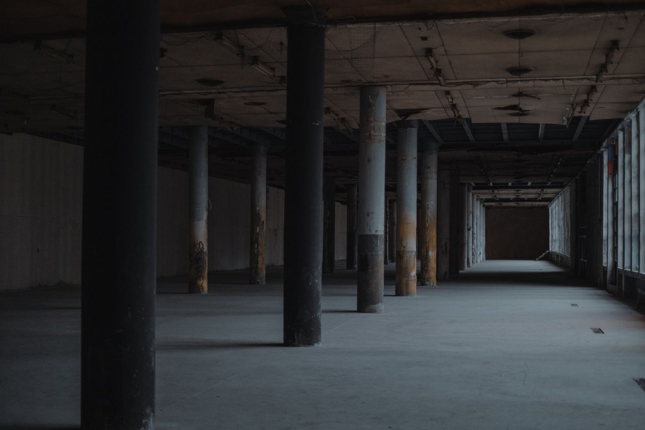 Perspective view of empty shabby spacious hall with columns in front of windows and exit in far side in semidarkness